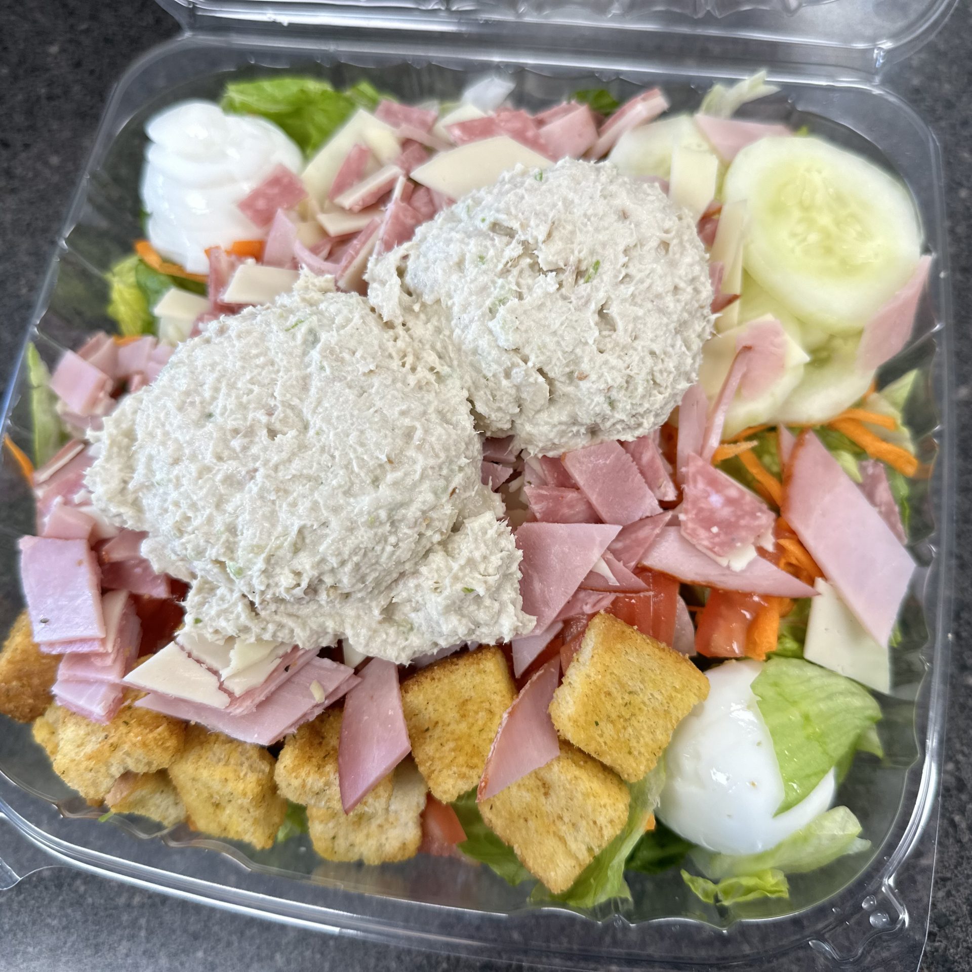 A salad with ham and croutons in a plastic container.
